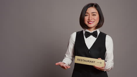 Asiatischer-Hotel-Concierge-Hält-Restaurantschild,-Um-Richtung-Anzugeben