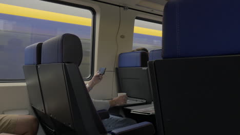 Blick-Auf-Männer-Im-Zug,-Die-Mit-Laptop-Auf-Dem-Tisch-Arbeiten-Und-Vor-Dem-Fenster-Trinken,-Niederlande