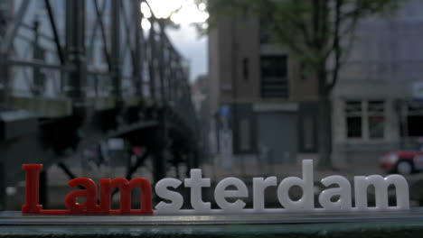 View-of-small-plastic-figure-of-Iamsterdam-letters-sculpture-on-the-bridge-against-blurred-cityscape-Amsterdam-Netherlands