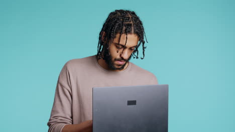 Man-inputting-data-on-laptop-while-standing-in-blue-studio-background