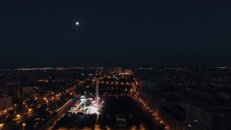 Luftnachtansicht-Des-Beleuchteten-Riesenrads-Im-Vergnügungspark-Vor-Dem-Himmel-Mit-Mond-Valencia,-Spanien