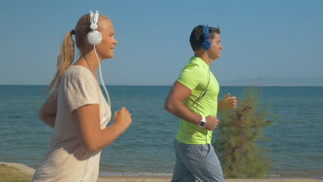 Couple-in-headphones-jogging-along-the-sea-front