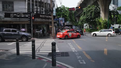 Orang-taxi-turn-left-from-the-street-with-the-stop-sign-on-as-other-vehicles-come-and-go-during-the-moment,-Pedestrian-Lane-on-Sukhumvit-26-across-is-Beethoven-tailoring,-Bangkok,-Thailand