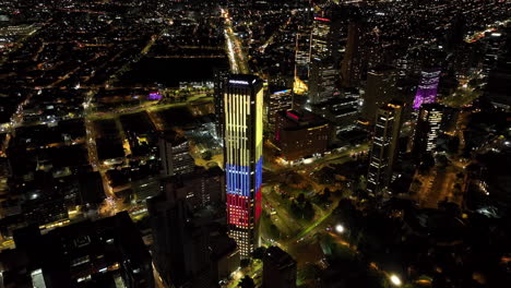 Aerial-view-orbiting-the-colorful-Colpatria-tower,-nighttime-in-downtown-Bogota,-Colombia