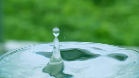 Droplet-of-water-creating-ripples-and-small-waves-in-a-glass-of-water-and-splattering-over-the-rim-of-the-container