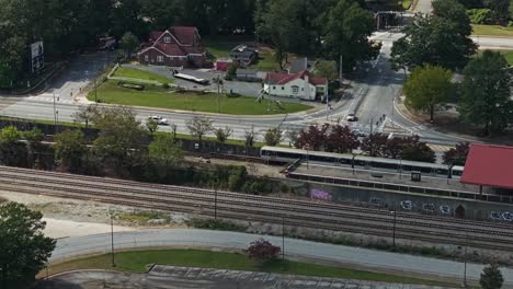 Aerial-top-down-shot-showing-departing-train-leaving-train-station-beside-road-with-driving-cars-in-Atlanta---tracking-shot-from-above