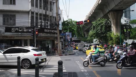 White-car-followed-by-a-lot-of-delivery-motorcycles-and-motor-taxis-during-a-red-walk-sign-and-traffic-red-stop-sign,-Pedestrian-Lane-on-Sukhumvit-26-across-is-Beethoven-tailoring,-Bangkok,-Thailand