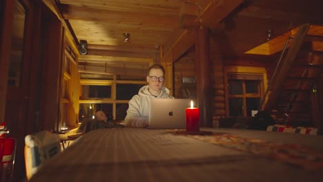 Son-work-at-laptop-while-father-sleep-in-background-at-cozy-wooden-cabin