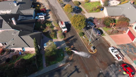 Working-on-a-fire-hydrant-in-Santa-Cruz---water-gushing-on-the-suburban-street---aerial-tilt-up-reveal