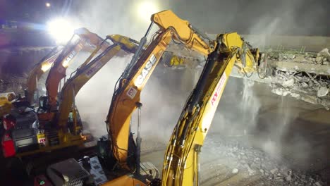 Un-Camión-Aéreo-De-Un-Equipo-De-Contratistas-Demoliendo-Un-Puente-De-Hormigón-Armado-Con-Excavadoras-De-Martillo-Neumático-Por-La-Noche,-Canadá