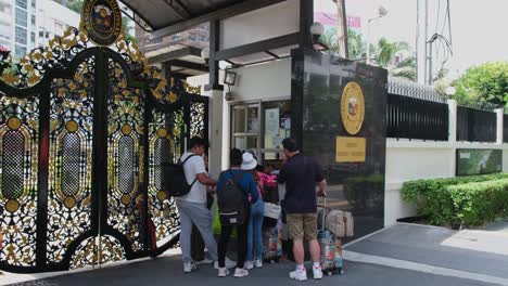 People-seen-from-behind-and-from-a-good-distance-showing-their-documents-to-enter-the-embassy,-Philippine-Embassy,-Sukhumvit-Road-corner-Soi-Philippines-Soi-30,1,-Bangkok,-Thailand