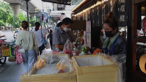 A-vendor-peeling-a-Papaya-and-one-chooses-which-fruit-to-buy,-Street-Food-along-Sukhumvit-Road-in-Bangkok,-Thailand