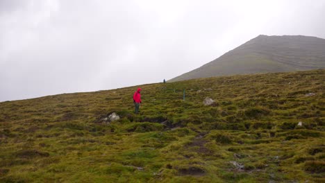 Female-hiker-walks-along-Villingardalsfjall-muddy-remote-path-in-Faroe-Islands