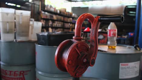 Shell-Hand-Crank-Fuel-Pump-seen-with-fuel-and-oil-barrels,-Auto-Repair-Shop,-Bangkok,-Thailand