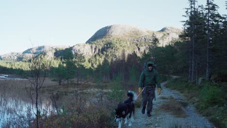 Hiker-With-His-Dog-On-Leash-Attached-On-His-Waist-Walking-In-The-Mountain-Track-To-The-Summit