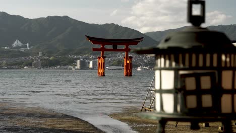 Background-Focus-View-Of-The-Grand-Floating-Torii-Gate-With-Foreground-Showing-Gently-Swaying-Hanging-Lantern-At-Itsukushima-Shrine
