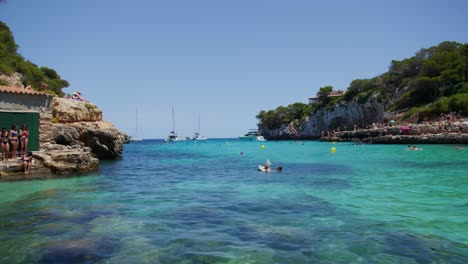 Mallorca:-Beach-Side-View-Of-Resort-In-Cala-Liombards-On-Majorca-Island,-Spain,-Europe-|-Three-Woman-on-Cliff