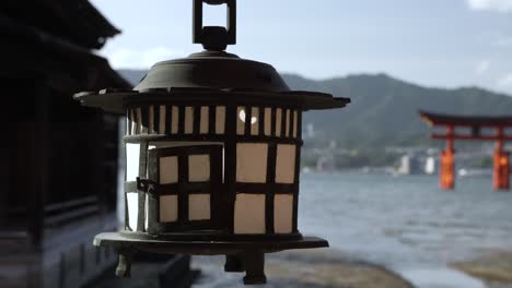 Gently-Swaying-Hanging-Lantern-At-Itsukushima-Shrine-With-Bokeh-Background-View-Of-The-Grand-Floating-Torii-Gate