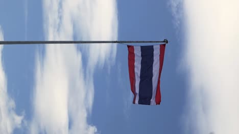 Aufnahmen-Im-Hochformat-Der-Thailändischen-Nationalflagge,-Die-Auf-Einem-Weißen,-Hohen-Stahlmast-Gehisst-Wird,-Der-Vom-Wind-Geblasen-Wird-Und-Vor-Dem-Hintergrund-Eines-Klaren-Blauen-Himmels-Und-Weißer-Wolken-Eine-Animierte-Welle-Erzeugt