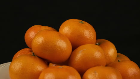 Plate-of-Clementine-oranges-rotates-isolated-on-black-background