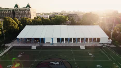 The-sun-sets-over-a-football-field,-casting-a-warm-glow-on-the-'Wolfpack'-logo,-with-event-preparations-in-the-background