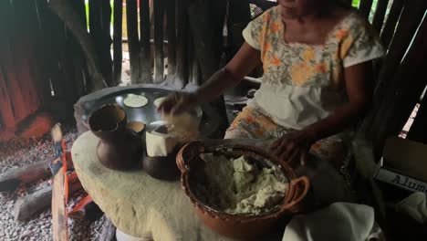 Mujer-Haciendo-Tortillas-De-Maíz-A-Mano-En-Su-Rústica-Cocina-Al-Aire-Libre-En-Un-Comal-Improvisado-Que-Utiliza-Una-Tapa-De-Barril-De-Aceite-Sobre-Un-Fuego-De-Madera-Abierto