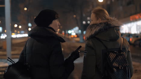 Two-women-talking-when-taking-walk-in-evening-winter-city