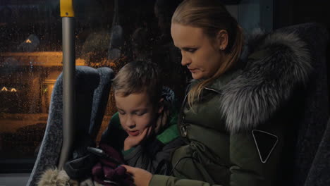 Niño-Con-Madre-Usando-Teléfono-Celular-En-El-Autobús