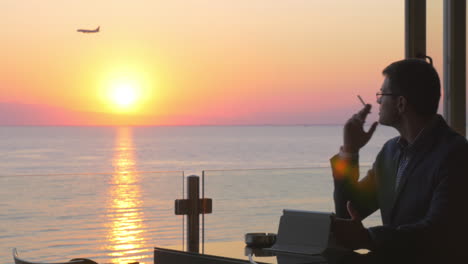 Smoking-businessman-with-pad-in-seaside-cafe-at-sunset