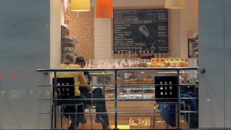 Dos-Mujeres-Hablando-En-La-Cafetería-Vista-Desde-Afuera