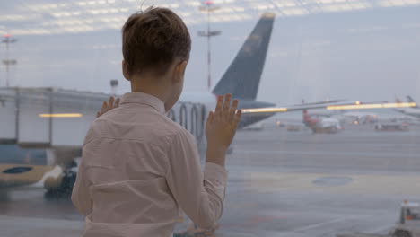 Niño-Esperando-El-Vuelo-Y-Mirando-Aviones-A-Través-De-La-Ventana