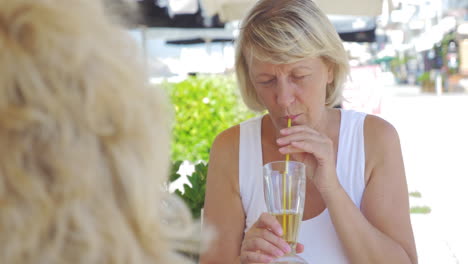 Amigas-Maduras-Tomando-Bebidas-Y-Hablando-En-Un-Café-Al-Aire-Libre