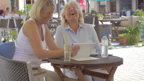 Mujeres-Viendo-Algo-Gracioso-En-Una-Tableta-En-Un-Café-Al-Aire-Libre