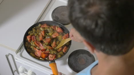 Man-stewing-tomatoes-mushrooms-and-potatoes-in-pan