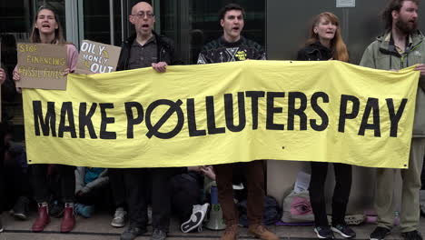 Five-protestors-stand-holding-a-large-yellow-banner-that-reads,-“Make-polluters-pay”-on-a-protest-calling-for-action-against-climate-change