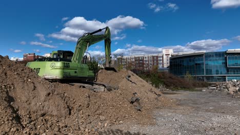 Eine-Niedrige-Winkelansicht-Eines-Lindgrünen-Baggers-Auf-Einer-Baustelle,-Auf-Einem-Erdhaufen,-An-Einem-Sonnigen-Tag-Mit-Blauem-Himmel