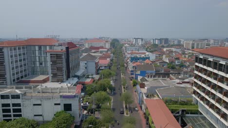 Vuele-Sobre-La-Calle-Principal-De-Tráfico-Con-Un-Edificio-De-Construcción-De-Rascacielos-En-La-Ciudad-De-Yogyakarta---Indonesia