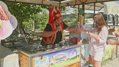 Türkischer-Eisverkäufer-Neckt-Spielerisch-Eine-Zufriedene-Kundin