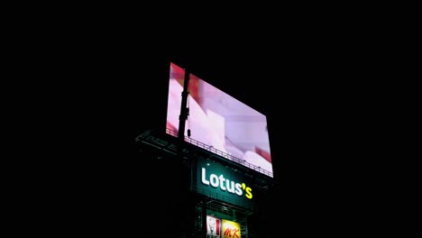 Big-LED-Billboard-at-a-Lotus's-super-market-in-Thailand-revealing-ads-like-KFC-and-ohers-while-a-boom-of-a-crane-moves-about,-Thailand