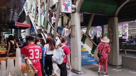 Camera-pans-to-the-left-revealing-the-BTS-Phrom-Phong-Station,-vendors-on-the-left,-and-people-going-up-and-down-the-stairs,-Sukhumvit,-Bangkok,-Thailand