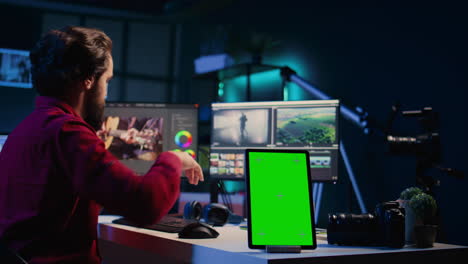 Green-screen-tablet-on-desk-in-studio-next-to-video-editor-arranging-recorded-stock-clips