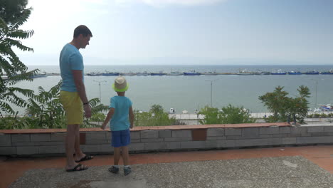 Young-man-and-son-are-throwing-rocks-against-boats-harbor-in-sea-Piraeus-Greece