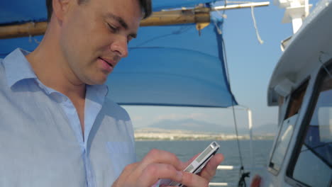 Der-Mann-Tippt-Auf-Seinem-Smartphone,-Während-Er-An-Einem-Sonnigen-Sommertag-Auf-Dem-Boot-Segelt