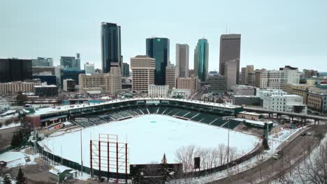 Eine-Filmische-4K-Drohnenaufnahme-Von-Wolkenkratzern-In-Der-Innenstadt,-Gebäuden,-Arena-Shaw-Park,-Baseball-Diamant,-Stadtlandschaft,-Winter-In-Der-Hauptstadt-Winnipeg,-Manitoba,-Kanada