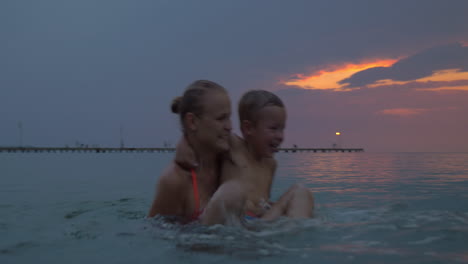 Bei-Sonnenuntergang-Schwimmt-Mutter-Mit-Sohn-Im-Meer-Der-Stadt-Perea-Griechenland