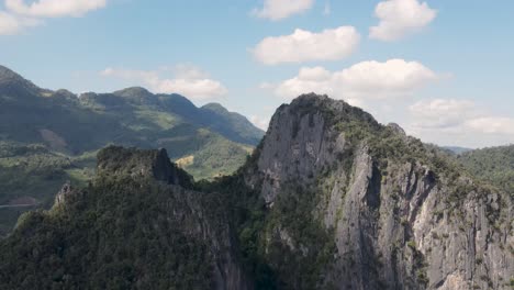 Aufsteigende-Luftaufnahme-Mit-Blick-Auf-Die-Hoch-Aufragenden-Bergklippen-In-Luang-Prabang-Und-Die-Bewaldete-Landschaft-Im-Hintergrund