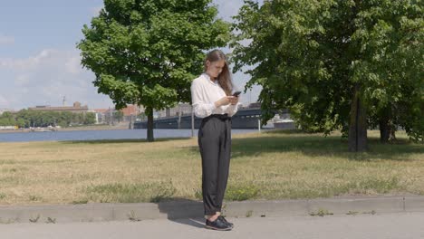 Business-woman-typing-on-smartphone-in-park-on-bright-sunny-day