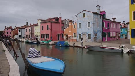 Colourful-fishermen-houses-and-boats-on-canal-on-cloudy-day,-Burano-Venice-Italy