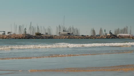 Slow-motion-shot-of-waves-crashing-on-Palavas-beach-with-a-marina-behind
