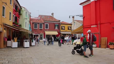 Tourists-visit-Burano-island,-street-with-shops-in-vivid-painted-houses,-Venice,-Italy